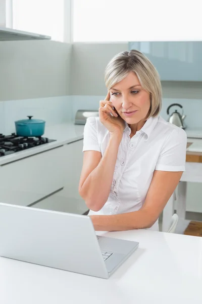 Mujer casual usando el ordenador portátil mientras está de guardia en la cocina —  Fotos de Stock