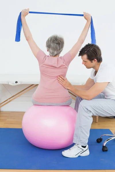 Старша жінка на м'ячі йоги з фізичним терапевтом — стокове фото