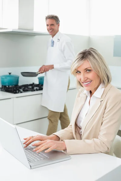 Femme utilisant un ordinateur portable et homme cuisinant des aliments — Photo