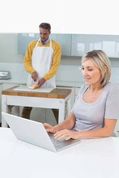 Woman with laptop and man chopping vegetables — Stock Photo, Image