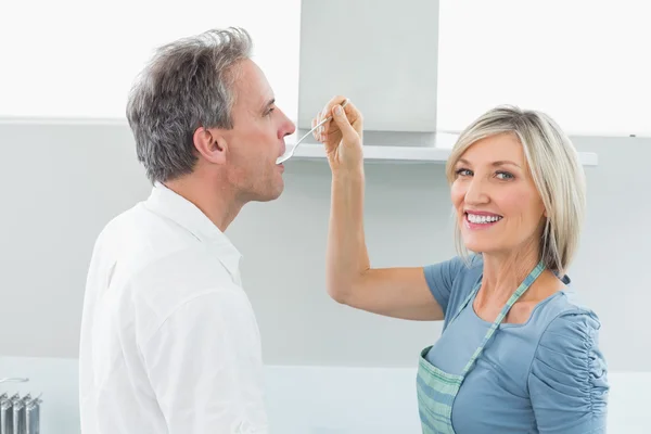 Mujer feliz alimentando al hombre en la cocina — Foto de Stock