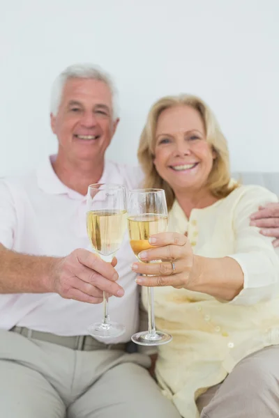 Senior couple holding out champagne flutes at home — Stock Photo, Image