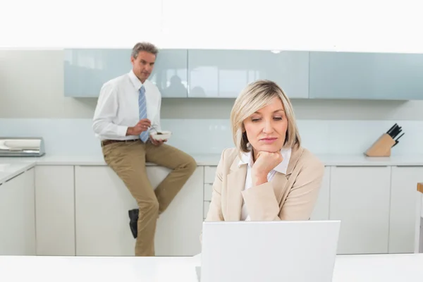 Woman using laptop and man in background at kitchen — Stock Photo, Image