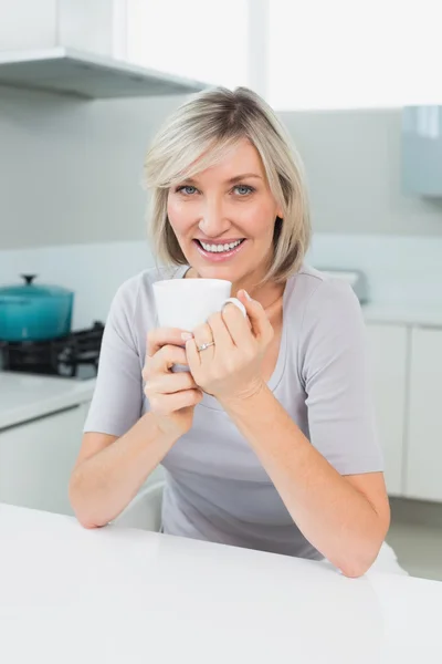Lachende casual vrouw met koffie beker in keuken — Stockfoto