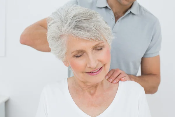 Fisioterapeuta masculino masajeando el cuello de una mujer mayor — Foto de Stock