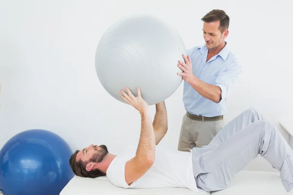 Physical therapist assisting man with yoga ball — Stock Photo, Image