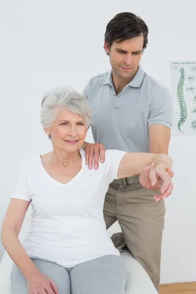 Fisioterapeuta masculino estirando el brazo de una mujer mayor — Foto de Stock