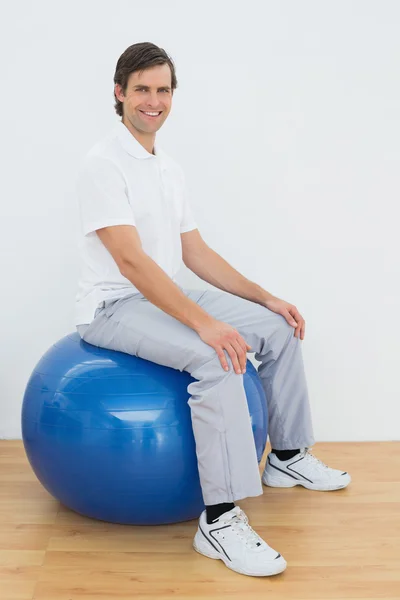 Smiling man sitting on exercise ball in hospital gym — Stock Photo, Image