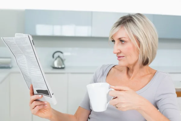 Mujer tomando café mientras lee el periódico en la cocina — Foto de Stock