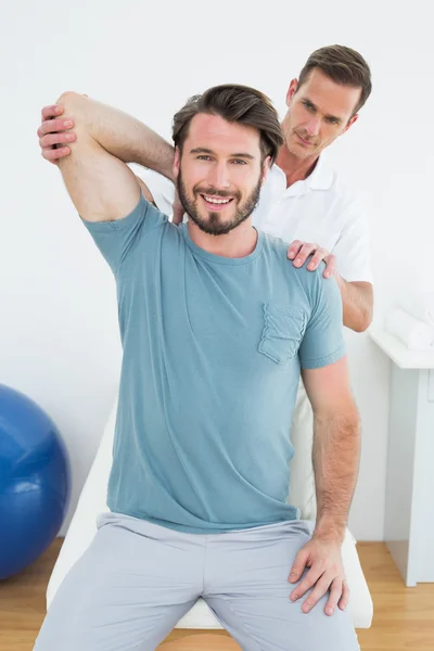 Mannelijke fysiotherapeut uitrekken een lachende man arm — Stockfoto