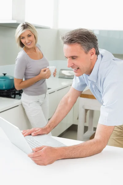 Hombre usando portátil con mujer en la cocina — Foto de Stock