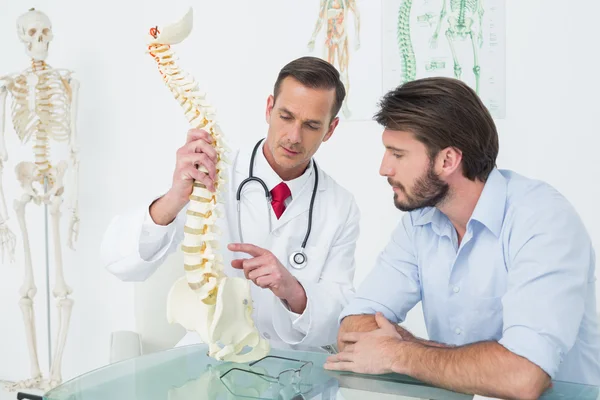 Médico masculino explicando a coluna vertebral a um paciente — Fotografia de Stock