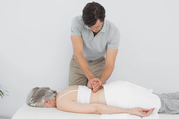 Fisioterapeuta masculino masajeando la espalda de una mujer mayor — Foto de Stock