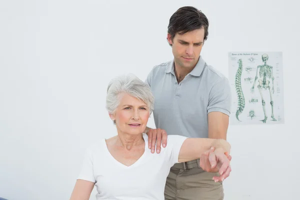Fisioterapeuta masculino esticando o braço de uma mulher idosa — Fotografia de Stock