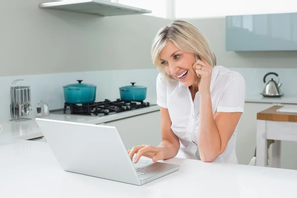 Mujer casual usando el ordenador portátil mientras está de guardia en la cocina — Foto de Stock