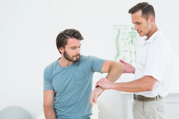 Genç bir adamın kolu inceleyerek erkek fizyoterapist — Stok fotoğraf