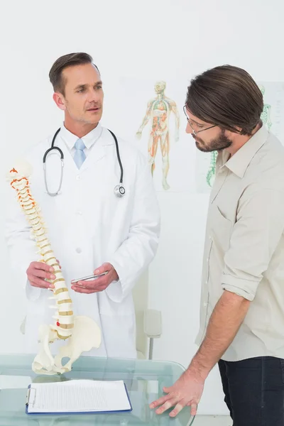 Médico masculino explicando a coluna vertebral a um paciente — Fotografia de Stock