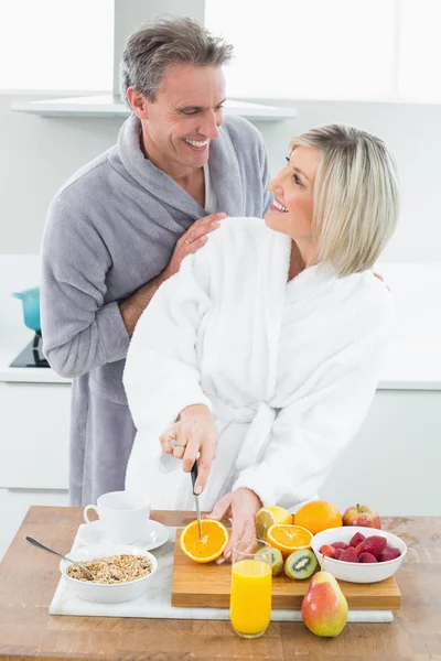 Man with a woman as she cuts fruits in kitchen — Stock Photo, Image