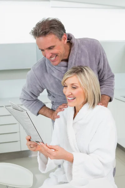 Couple in bathrobes reading newspaper in kitchen — Stock Photo, Image