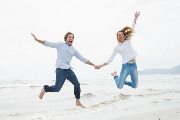 Glad par hålla händer och hoppning på stranden — Stockfoto