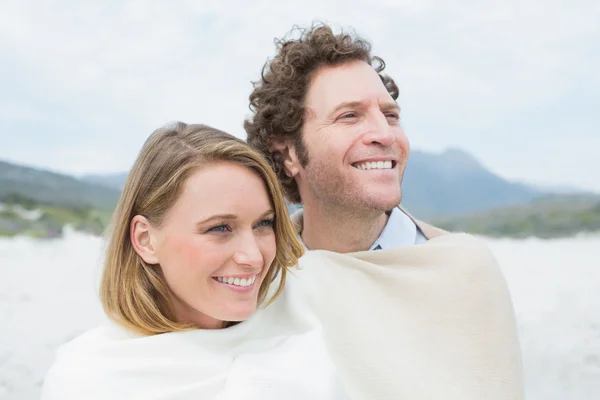 Couple souriant enveloppé dans une couverture à la plage — Photo