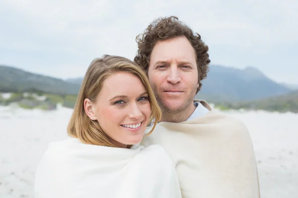 Cuplu zâmbitor înfășurat în pătură la plajă — Fotografie, imagine de stoc