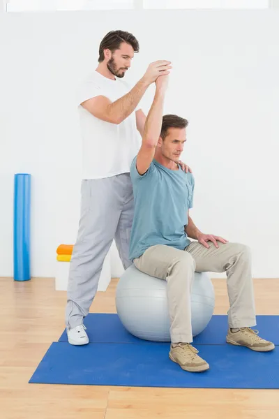 Man on yoga ball working with a physical therapist — Stock Photo, Image