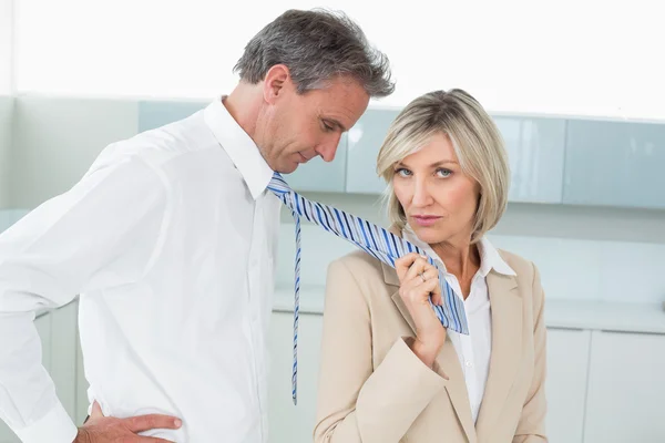 Woman holding a man by his neck tie in kitchen — Stock Photo, Image