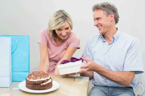 Man giving a happy woman a birthday gift beside cake — Stock Photo, Image