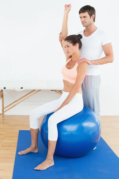 Жінка на м'ячі йоги під час роботи з фізіотерапевтом — стокове фото