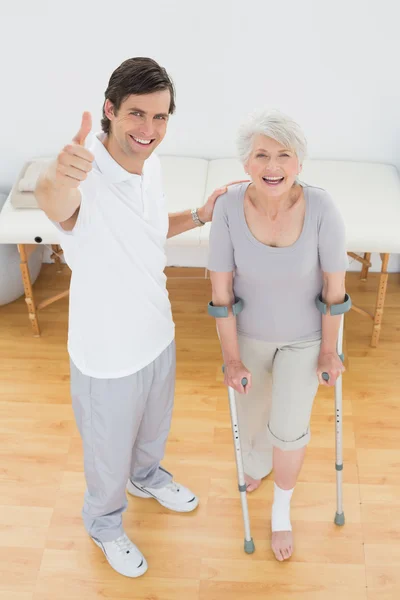 Terapeuta gestos pulgares hacia arriba con el paciente discapacitado senior — Foto de Stock