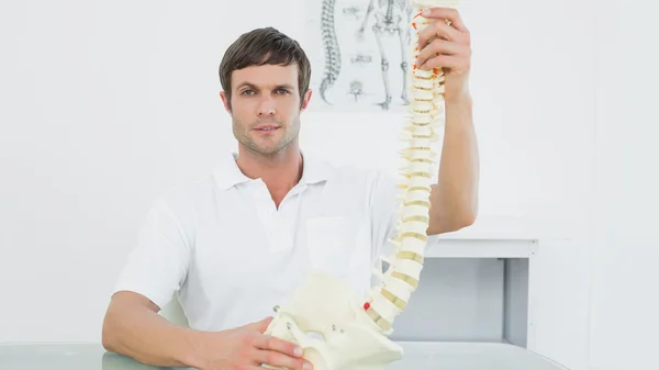 Confiado doctor sosteniendo esqueleto modelo en su oficina — Foto de Stock