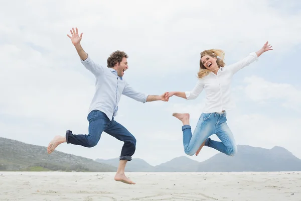 Cheerful couple holding hands and jumping at beach — Stock Photo, Image