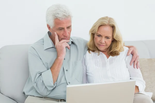 Casal de idosos relaxado usando laptop no sofá — Fotografia de Stock