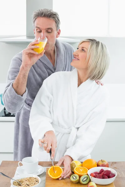 Uomo che beve succo d'arancia e donna che taglia frutta in cucina — Foto Stock