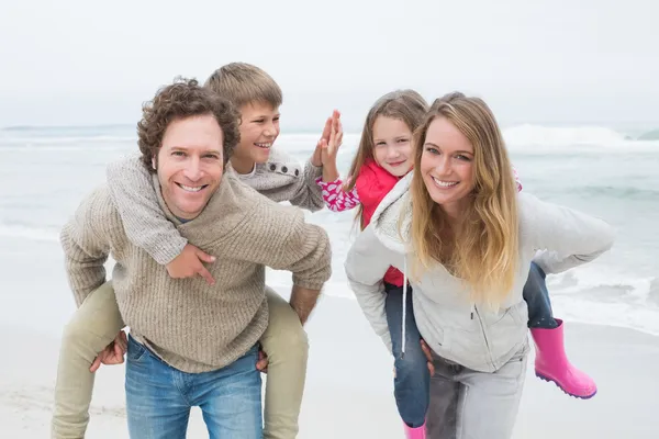 Lyckliga paret åker snålskjuts barnen på stranden — Stockfoto