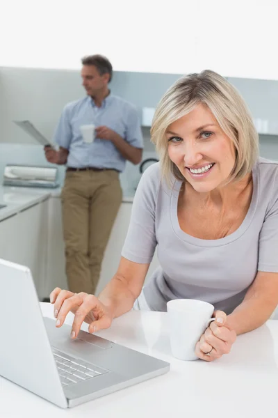 Mujer usando portátil y hombre leyendo periódico en la cocina — Foto de Stock