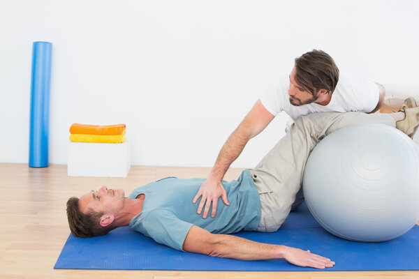 Физиотерапевт помогает молодому человеку с мячом для йоги
