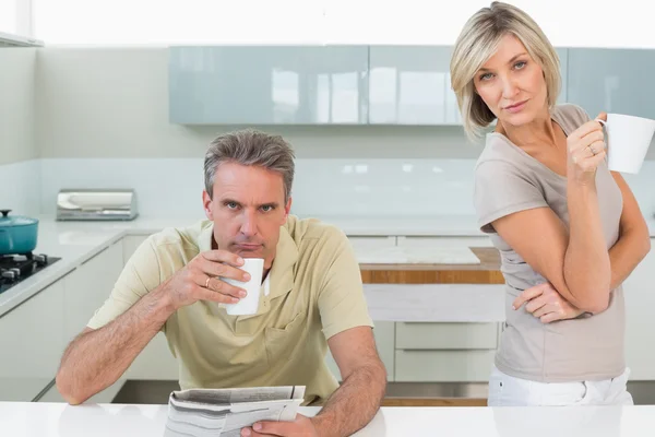 Serious couple with coffee cups and newspaper in kitchen — Stock Photo, Image