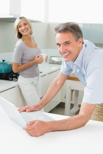 Homem usando laptop com mulher na cozinha — Fotografia de Stock