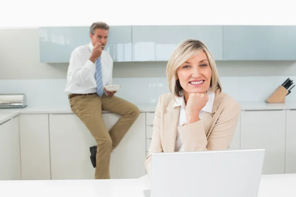 Mujer sonriente con portátil y hombre de fondo en la cocina — Foto de Stock