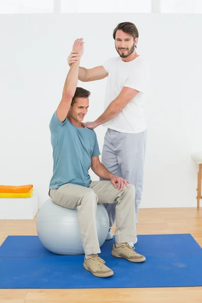 Man on yoga ball working with a physical therapist — Stock Photo, Image