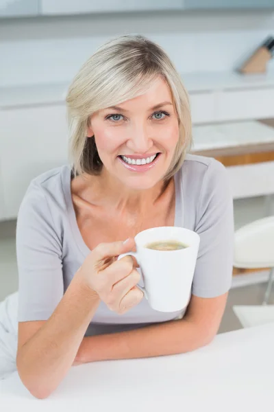 Smiling young woman with coffee cup in kitchen — Stock Photo, Image