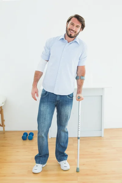 Full length portrait of a smiling man with crutch — Stock Photo, Image