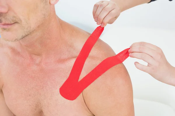 Hands putting on red kinesio tape on patient's shoulder — Stock Photo, Image