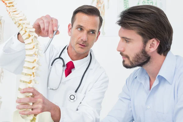 Médico masculino explicando a coluna vertebral a um paciente — Fotografia de Stock