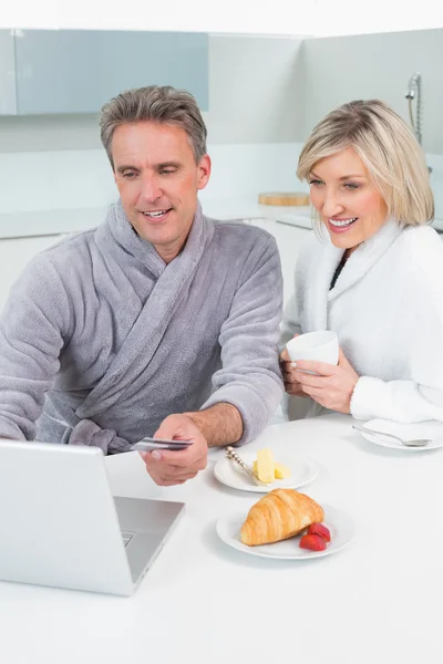 Pareja en albornoces con ordenador portátil en la cocina — Foto de Stock