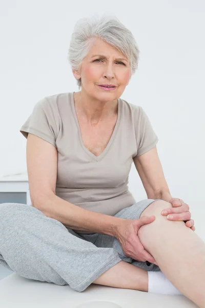 Старша жінка з болючим коліном сидить на обстежувальному столі — стокове фото