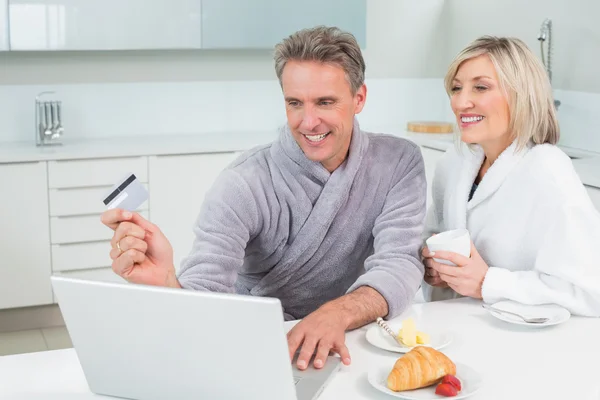Couple in bathrobes doing online shopping in kitchen — Stock Photo, Image