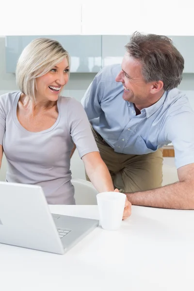 Happy casual couple using laptop in kitchen — Stock Photo, Image